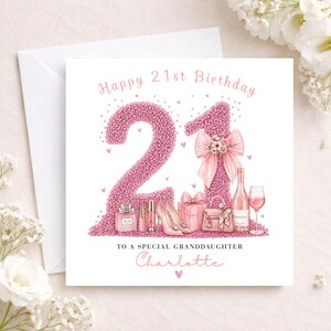 May include: A white greeting card with a pink glitter design that says "Happy 21st Birthday". The number "21" is in pink glitter, with illustrations of a perfume bottle, high heels, and a wine bottle.