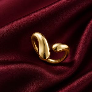 May include: A polished gold-tone ring featuring an open, bypass-style design with two smooth, rounded, teardrop-shaped ends that curve towards each other, creating a fluid, continuous metallic form with a high-shine, reflective surface finish.