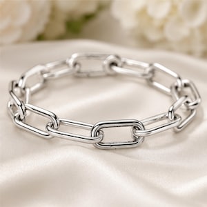 May include: A polished silver-tone chain link bracelet featuring a series of uniform, elongated oval links connected in a continuous loop. The metal surface has a high-shine, reflective finish that catches the light, creating a smooth, metallic appearance.