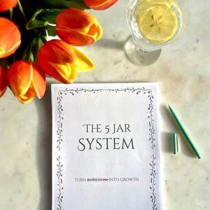 May include: A still-life image featuring a bouquet of orange and yellow tulips, a glass of water with lemon slices, and a notebook with the text "THE 5 JAR SYSTEM". A green pen and cap are also present.