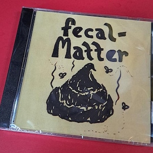 May include: A CD case with a yellow cover featuring the words "fecal-Matter" in black, stylized lettering. Below the text is a black illustration of a pile of feces with flies. The CD case is in a clear plastic sleeve.