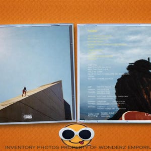 Puede incluir: Una caja de CD con dos paneles. El panel frontal muestra a una persona caminando sobre un edificio con un cielo azul de fondo. El panel trasero presenta el perfil de una persona con rastas. El texto es visible en ambos paneles.