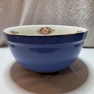 May include: A blue ceramic mixing bowl with a floral design. The bowl has a wide rim with a gold edge and a cream-colored interior. Pink and white flowers are arranged around the rim.
