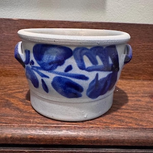 May include: A ceramic planter with a light gray base and rim, adorned with blue floral patterns. It features two small handles and is suitable for indoor or outdoor use. The planter is approximately 6 inches in diameter and 5 inches tall.