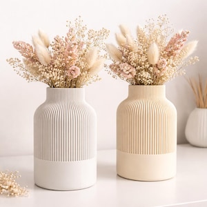 Könnte beinhalten: Ein Set aus drei Keramikbechern mit gesprenkelter, matter Oberfläche. Die Becher sind in Creme-, Hellgrau- und Dunkelgrautönen gehalten. Jeder Becher hat ein schlichtes, minimalistisches Design und einen abgerundeten Henkel.