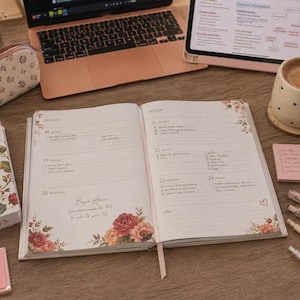 May include: An open planner with floral detailing and the text "Begin Again". A laptop, tablet, and coffee cup are on the wooden surface. Pens, sticky notes, and highlighters are arranged around the planner.