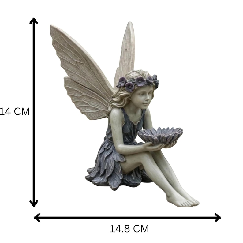 K&ouml;nnte beinhalten: Eine sitzende Feenfigur, etwa 14 cm hoch und 14,8 cm breit, mit gro&szlig;en, detaillierten Fl&uuml;geln. Die Fee tr&auml;gt ein blau-graues Kleid und einen Blumenkranz und h&auml;lt eine bl&uuml;tenf&ouml;rmige Schale. Die Statue besteht aus einem stein&auml;hnlichen Material.