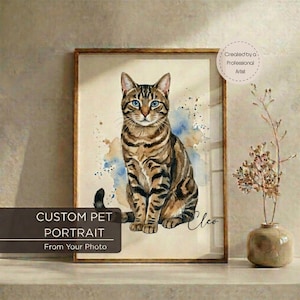 May include: Custom pet portrait of a brown tabby cat with blue eyes, watercolor style. The artwork is framed in a wooden frame and includes the text "Custom Pet Portrait From Your Photo". The cat's name, "Cleo", is written in cursive.