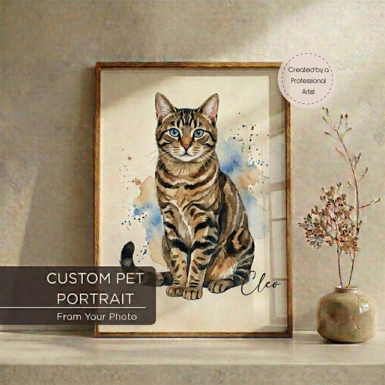 May include: Custom pet portrait of a brown tabby cat with blue eyes, watercolor style. The artwork is framed in a wooden frame and includes the text "Custom Pet Portrait From Your Photo". The cat's name, "Cleo", is written in cursive.