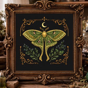 Può includere: Un ricamo a punto croce incorniciato con un disegno di falena verde e oro su sfondo nero. La cornice è ornata, con finitura oro scuro. L'immagine include una luna crescente e dettagli floreali. Il tema generale è gotico e mistico.