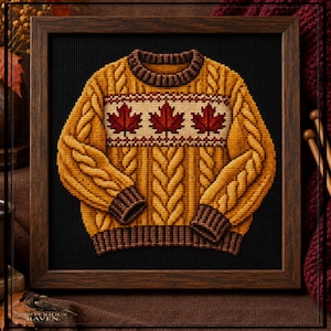 May include: A cross-stitch embroidery of a mustard yellow cable-knit sweater featuring a horizontal band with three dark red maple leaves. The sweater has a dark brown ribbed collar, cuffs, and hem, all framed in a dark wood square frame.
