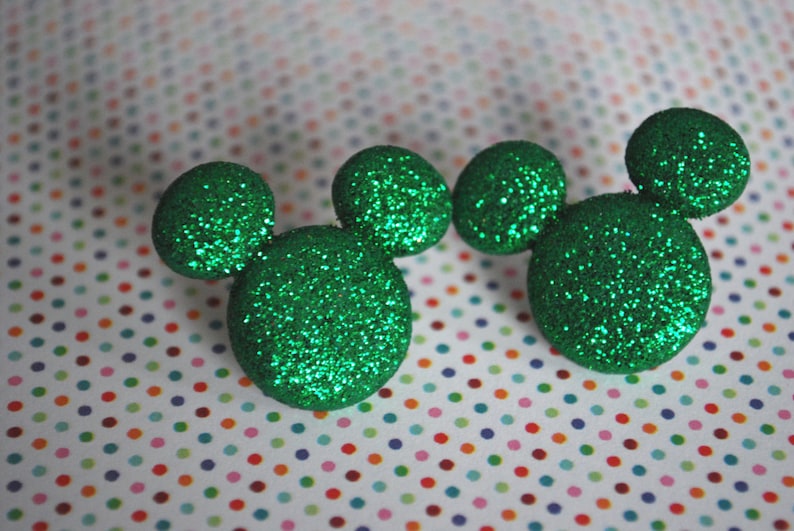 May include: Two green glitter Mickey Mouse ears. The ears are made of a soft, sparkly material and are perfect for adding a touch of Disney magic to any outfit.