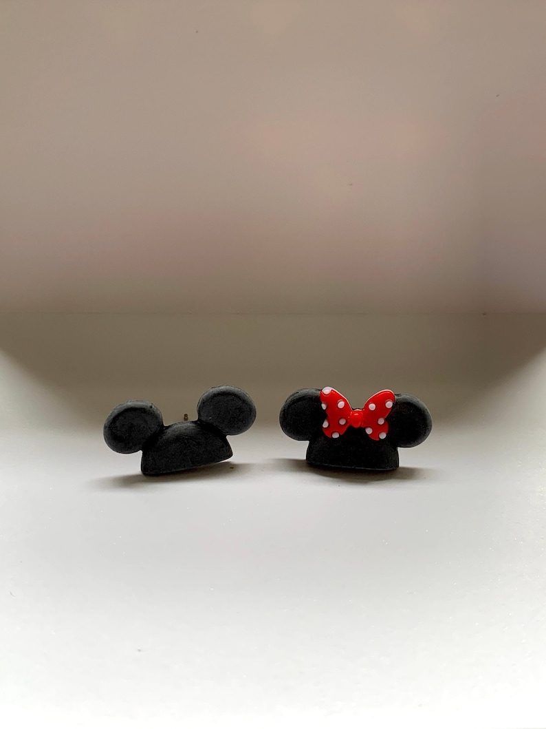 May include: A pair of black Mickey Mouse ears with a red bow with white polka dots on one ear.