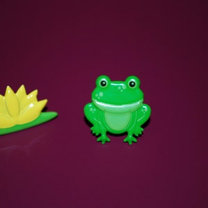 May include: A green frog with a wide smile and a yellow lily pad.