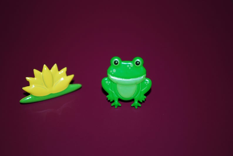 May include: A green frog with a wide smile and a yellow lily pad.