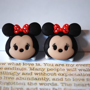 May include: Two black and brown cartoon character charms with red bows and white polka dots. The characters have large eyes and a small nose.