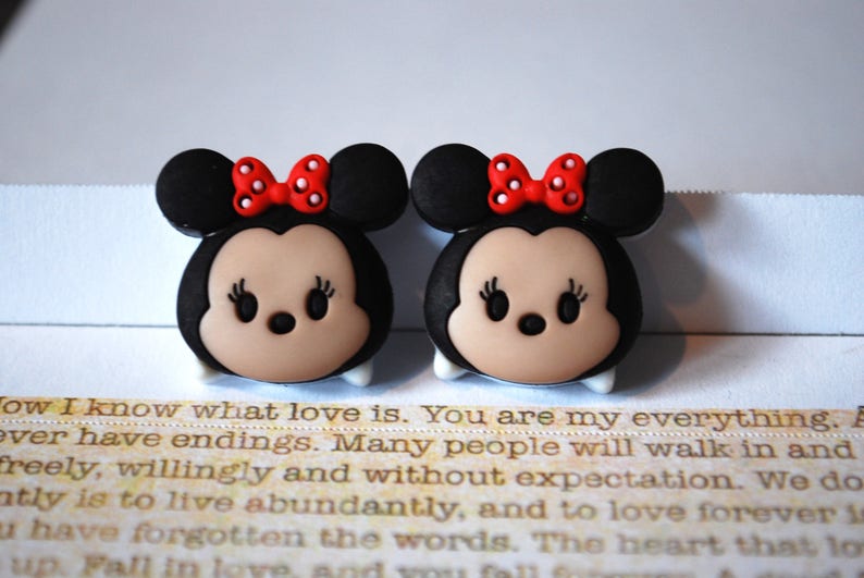 May include: Two black and brown cartoon character charms with red bows and white polka dots. The characters have large eyes and a small nose.