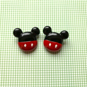 Op de afbeelding: Twee zwarte en rode Mickey Mouse-knoppen met witte ogen.