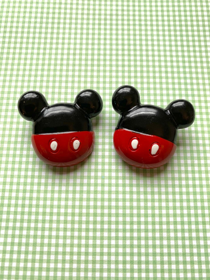 Op de afbeelding: Twee zwarte en rode Mickey Mouse-knoppen met witte ogen.
