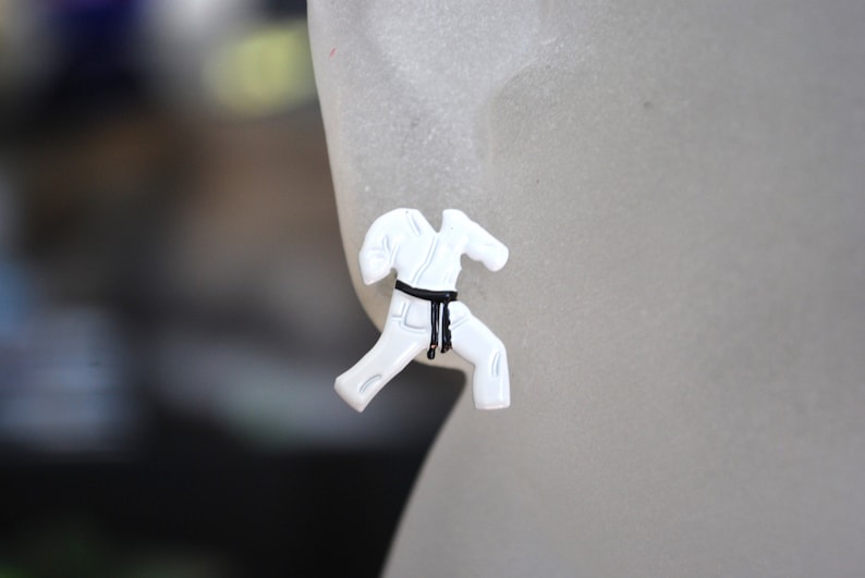 May include: White karate uniform earrings with a black belt. The earrings are in the shape of a person in a karate stance.