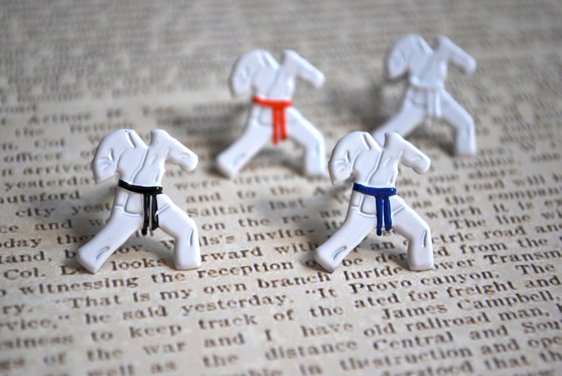 May include: Four white karate figurines in a fighting stance. The figurines are wearing white karate uniforms with black, red, and blue belts.