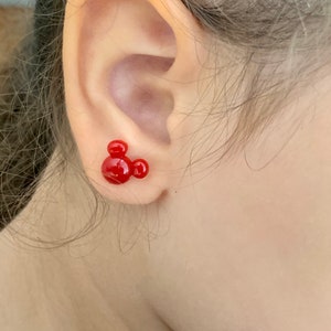 May include: Red Mickey Mouse stud earrings. The earrings are small and feature a classic Mickey Mouse silhouette.