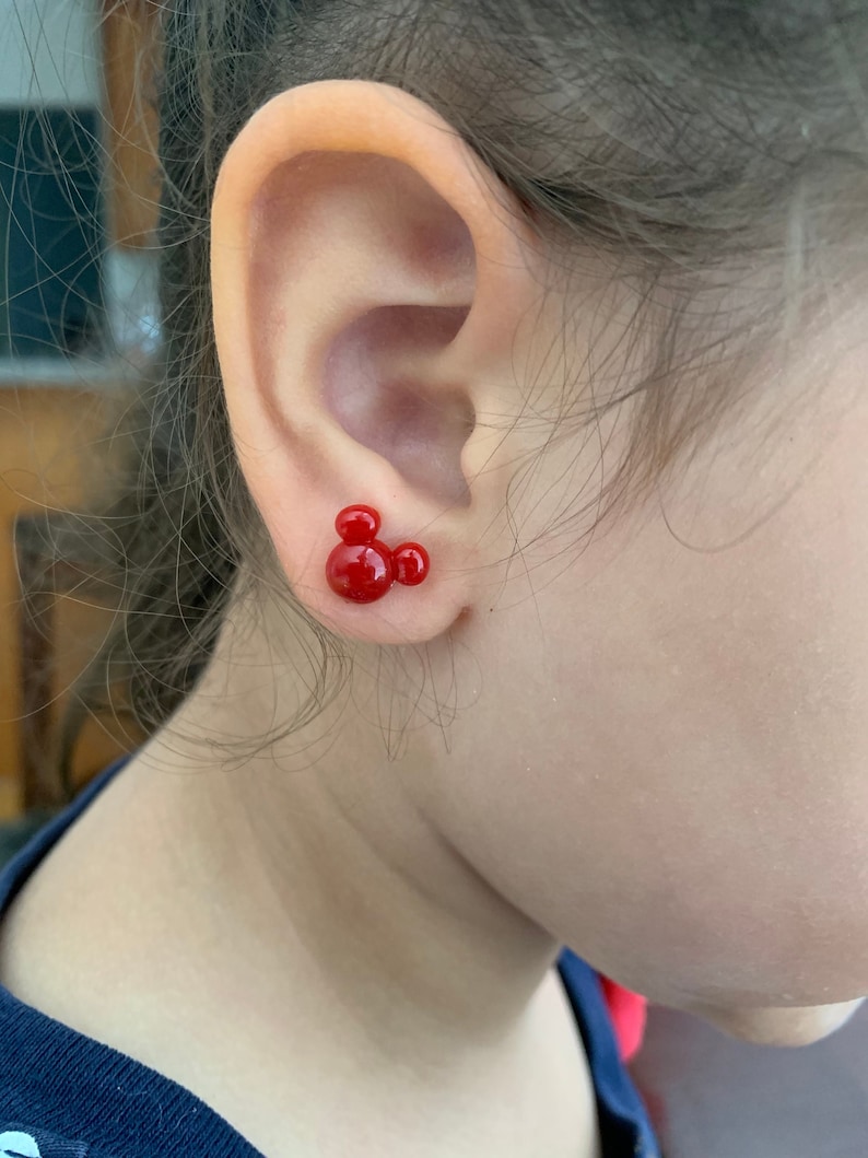 May include: Red Mickey Mouse stud earrings. The earrings are small and feature a classic Mickey Mouse design.