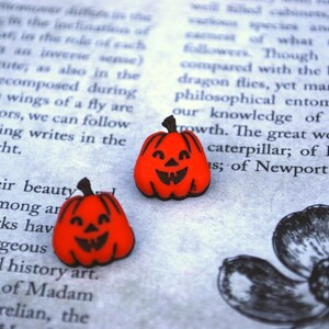 May include: Two small orange pumpkin-shaped Halloween decorations with black painted faces. The pumpkins are on a page of a book.