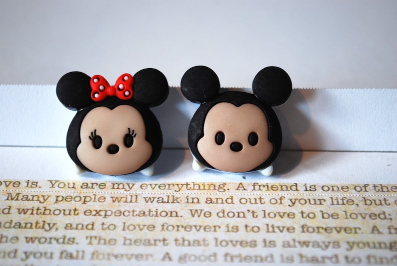 May include: Two small, cartoon-style figurines of Mickey Mouse and Minnie Mouse. Mickey is wearing black ears and a black and white face. Minnie is wearing black ears, a red bow, and a black and white face.