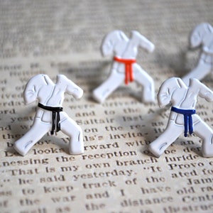 May include: Three white karate figurines with black, red, and blue belts. The figurines are posed in a karate stance and are on a white background.