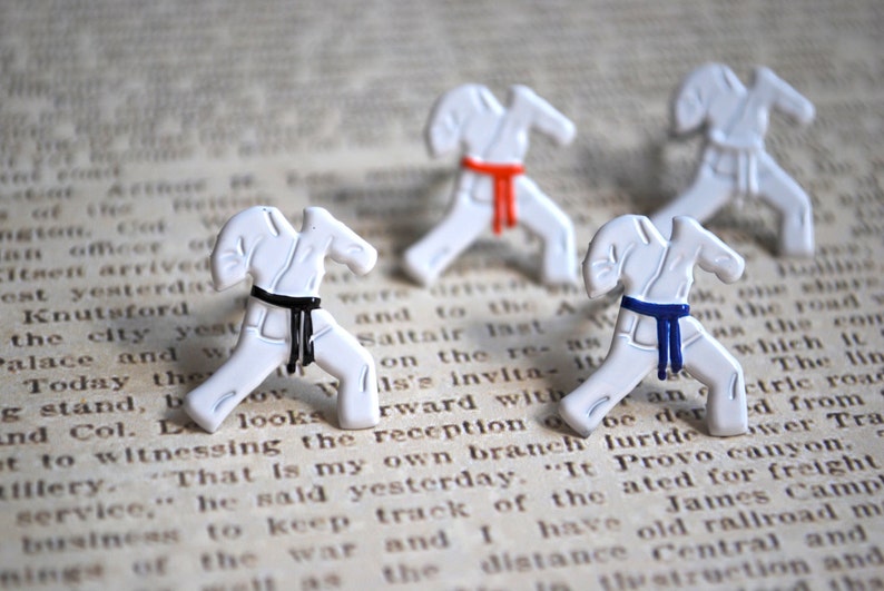 May include: Three white karate figurines with black, red, and blue belts. The figurines are posed in a karate stance and are on a white background.