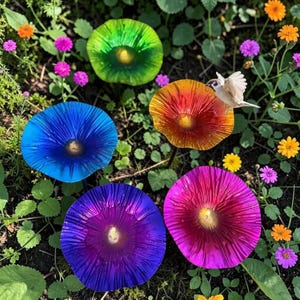 Puede incluir: Vista cenital de cinco coloridas setas de aspecto vítreo en tonos azul, verde, naranja, morado y rosa. Están rodeadas de pequeñas flores y vegetación, con un pequeño pájaro posado en una de ellas. Setas decorativas.