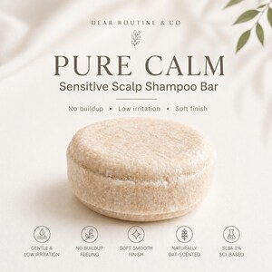 May include: A round, beige shampoo bar with the text "PURE CALM Sensitive Scalp Shampoo Bar". The bar is labeled as gentle, low irritation, and naturally oat-scented. Additional text includes "No buildup" and "Soft finish".