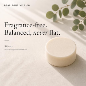May include: A round, off-white conditioner bar with the text "Fragrance-free. Balanced, never flat." and "Silence Nourishing Conditioner Bar." The product is displayed on a neutral background with eucalyptus leaves.