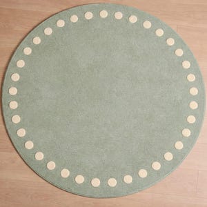 May include: A circular rug in a pale blue hue, featuring a decorative border of cream-colored circles. The rug is made from a soft material, ideal for a nursery or playroom. The rug has a diameter of approximately 122 cm.