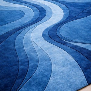Könnte beinhalten: Ein blauer Teppich mit einem fließenden, wellenartigen Design. Der Teppich hat Blautöne, die einen strukturierten, geschichteten Effekt erzeugen. Der Teppich besteht aus einem weichen Material und eignet sich für Wohn- oder Schlafzimmer. Maße in Zentimetern.