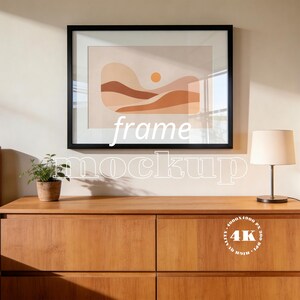 Könnte beinhalten: Ein gerahmter Kunstdruck mit schwarzem Rahmen, der eine abstrakte Landschaft in warmen Erdtönen zeigt. Das Kunstwerk hängt über einer Holzkommode, mit einer kleinen Topfpflanze und einer Lampe mit beigem Schirm. Die Worte "frame mockup" sind überlagert.