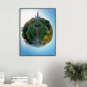 May include: A framed print featuring a spherical view of a park with a cathedral and surrounding buildings. The image has a blue sky and a bright sun. The park has green grass and trees. The print is in a black frame.