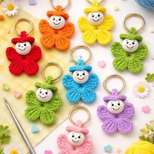 May include: A collection of handmade crochet keychains in various colors, including red, orange, yellow, green, blue, and purple. Each keychain features a smiling face and a flower-shaped design, with a gold-colored ring for attachment.