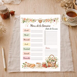 May include: A weekly menu and shopping list planner with floral and strawberry illustrations. The planner includes sections for each day of the week, a shopping list, and notes. A pen, tea cup, and jam jar are also visible.