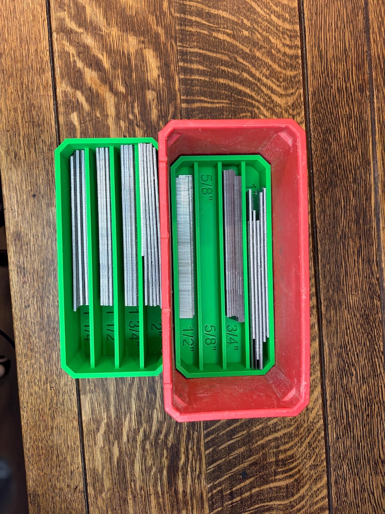 May include: A red and green plastic organizer with various sizes of metal pins. The organizer is open, revealing the pins arranged in rows. The sizes are labeled as 1/2", 5/8", 3/4", 1", 1 1/2", 1 3/4", and 2".