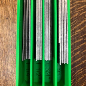 May include: A green plastic organizer holding several metal files. The files are labeled with their widths: 1 1/4", 1 1/2", 1 3/4", and 2". The files are arranged vertically within the organizer.