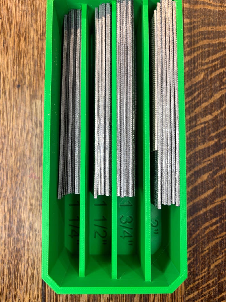 May include: A green plastic organizer holding several metal files. The files are labeled with their widths: 1 1/4", 1 1/2", 1 3/4", and 2". The files are arranged vertically within the organizer.