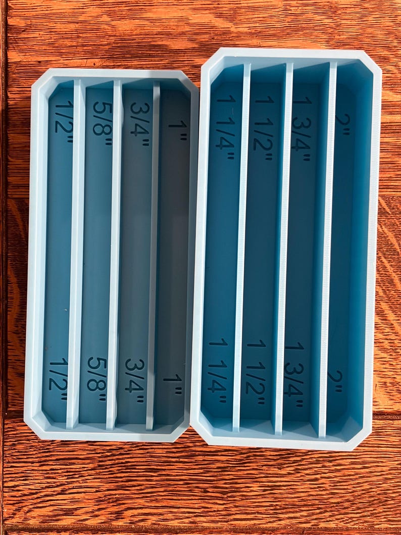 May include: Two rectangular, teal-colored resin molds with vertical dividers. The molds are labeled with inch measurements: 1/2", 5/8", 3/4", 1", 1 1/4", 1 1/2", 1 3/4", and 2". The molds are designed for crafting or creating items.