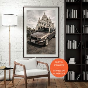 Puede incluir: Impresión enmarcada que presenta un coche marrón vintage frente a la Basílica del Sacré-Cœur en París. La imagen tiene un tono sepia, con la matrícula del coche visible. La impresión se muestra en un salón.