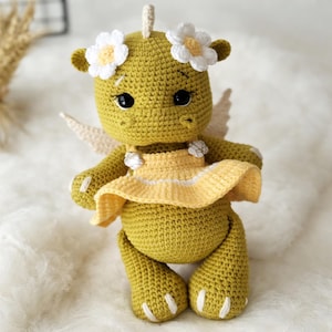 May include: A handmade crochet dragon doll in shades of yellow-green, wearing a yellow dress and white flower accents. The dragon has small wings and black eyes. The doll is approximately 7 inches tall.
