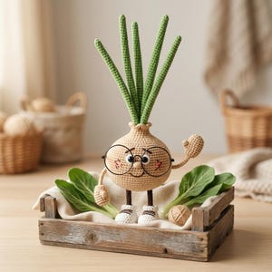 Puede incluir: Una figura de cebolla tejida a ganchillo con cuerpo redondo beige, pelo en forma de brotes verdes y gafas de montura negra. La figura tiene brazos pequeños, piernas marrones y zapatos blancos, con mejillas rosadas, dentro de una caja de madera.