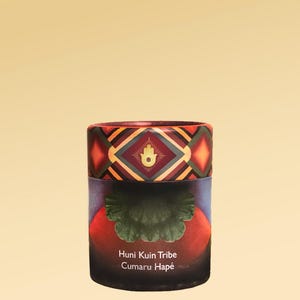 Könnte beinhalten: Zylindrischer Behälter mit einem geometrischen Muster in Rot, Orange und Braun. Die Oberseite zeigt ein Rautenmuster mit einem Handsymbol. Auf dem Etikett steht "Huni Kuin Tribe Cumaru Hapé."