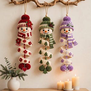 May include: Three hanging snowman ornaments with crocheted bodies and spiral tails. The left snowman wears red, the middle green, and the right purple. Each features a matching knit hat, scarf, and decorative accents like flowers, trees, and snowflakes.