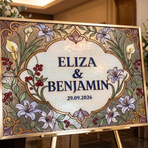 May include: A rectangular sign with a gold frame featuring a stained glass design of purple and yellow lilies with red berries. The center panel displays the text ELIZA & BENJAMIN and the date 29.09.2026 in dark blue lettering on a cream background.